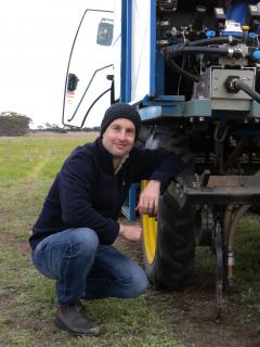 Daniel Huberli crouches near a tractor in a paddock